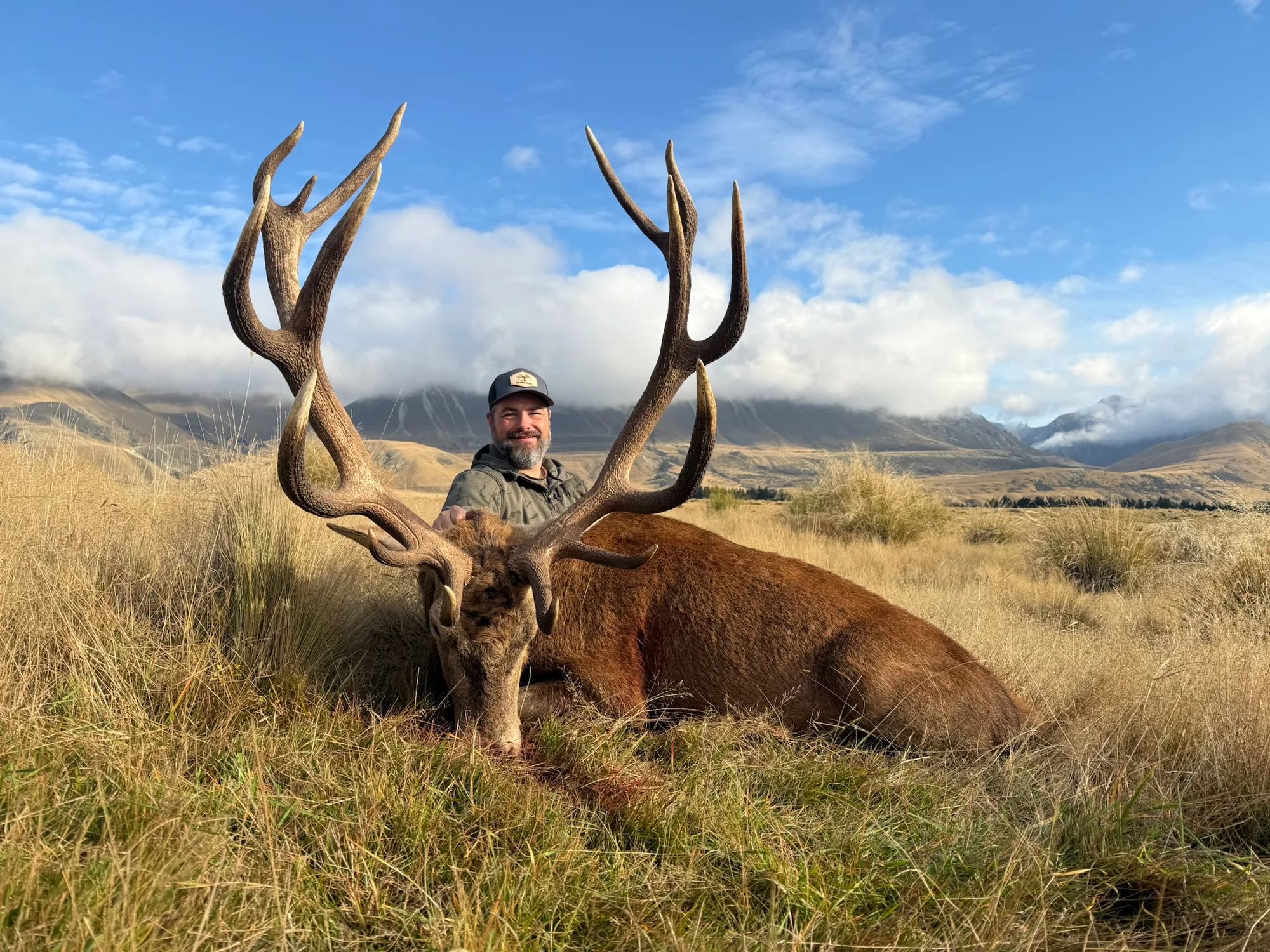 Hunter with a red stag beneath New Zealand mountains